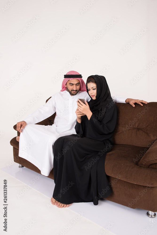 Arab muslim married couple using smart phone while sitting on sofa chair at home Arab muslim married couple using smart phone while sitting on sofa chair at home