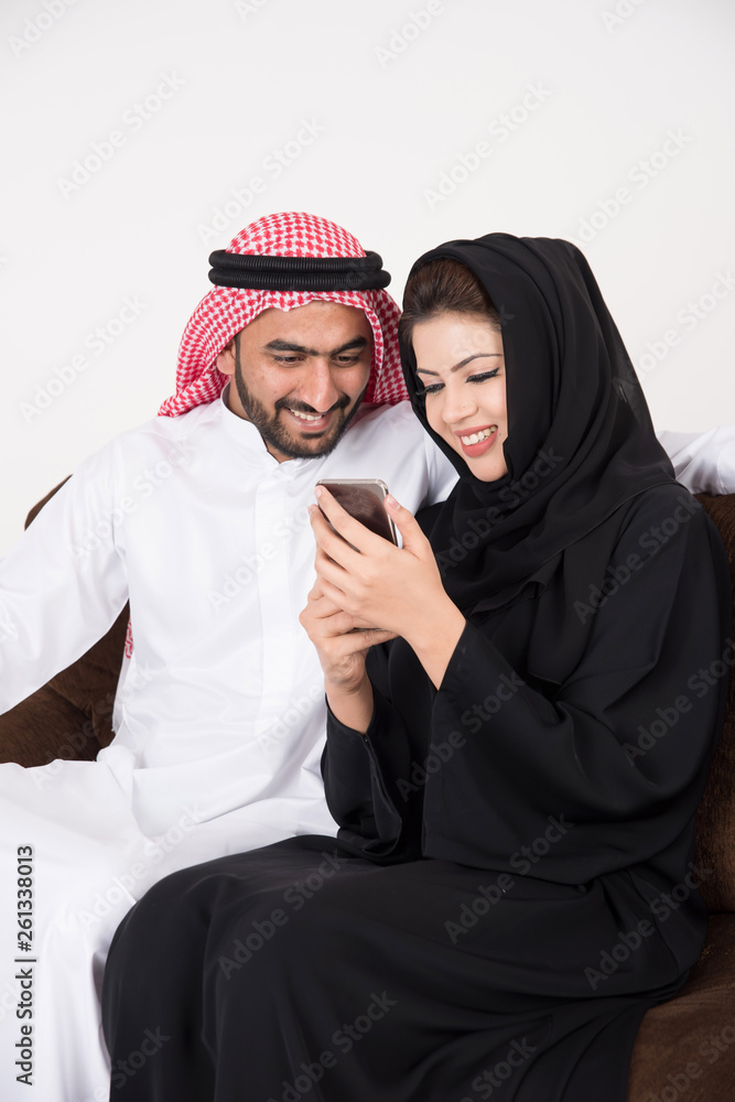 Arab muslim married couple using smart phone while sitting on sofa chair at home Arab muslim married couple using smart phone while sitting on sofa chair at home