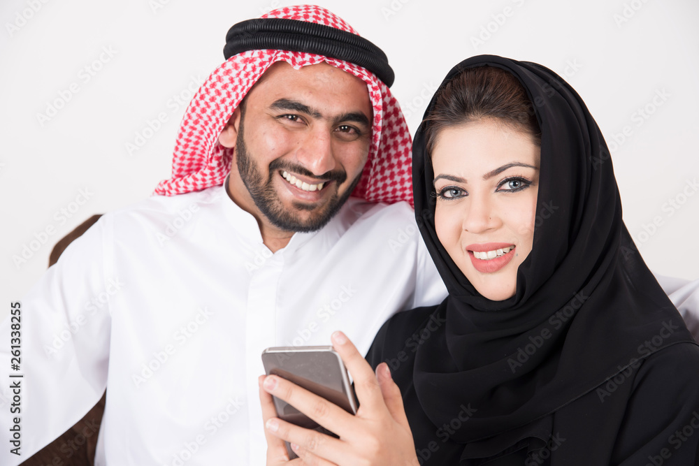 Arab muslim married couple using smart phone while sitting on sofa chair at home Arab muslim married couple using smart phone while sitting on sofa chair at home