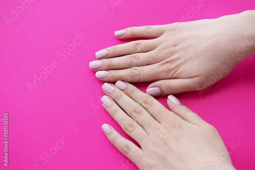 Manicured hands on pink background. Hands with manicured nails colored with beige nail polish.