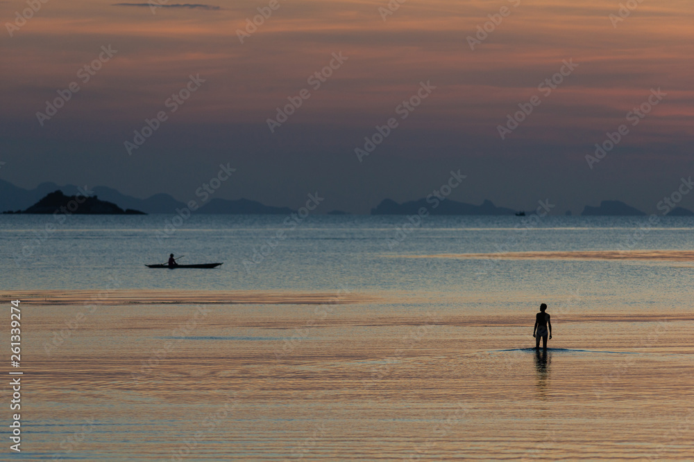 Fisherman standing on a low tide at evening sky background in the sea water
