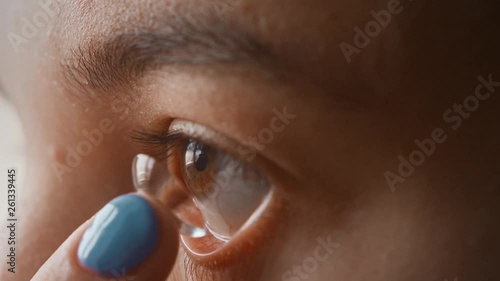 A beautiful young girl puts contact lenses in her eye close-up, macro. Blinking distributes the lens in the pupil. Brown eyes, black eyelashes, transparent lenses. Slow motion, 4K