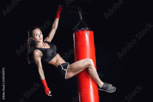 Fitness concept. Boxer female athlete holding onto punching bag. Black isolated background