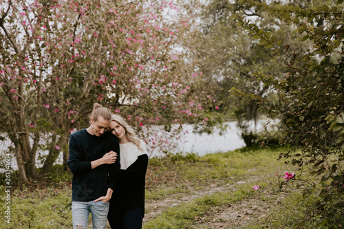 Young Couple in Love Holding One Another Outside in Nature in From of Cherry Blossom Tree and Pond © MeganMahoneyPhotos