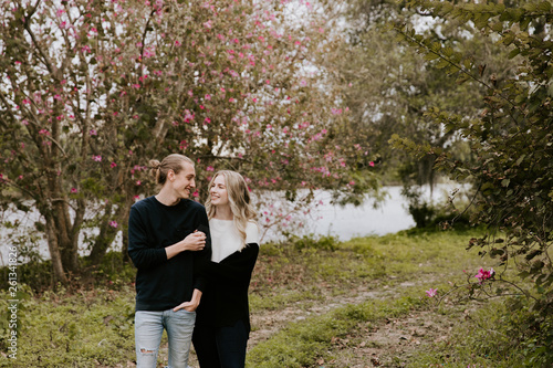 Young Couple in Love Holding One Another Outside in Nature in From of Cherry Blossom Tree and Pond © MeganMahoneyPhotos