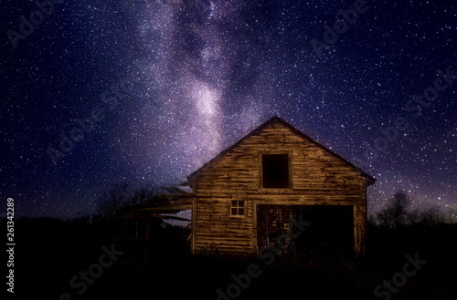 A crumbling wooden car garage under a star filled night sky in a rural landscape