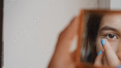 Reflection in the mirror of a beautiful young girl who wears contact lenses in her eye close-up. Blinking distributes the lens in the pupil. Brown eyes, transparent lenses. Slow motion, 4K
