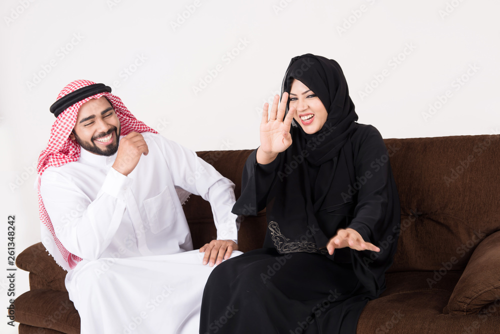 Arab couple enjoying and laughting while sitting on sofa chair at home Arab couple enjoying and laughting while sitting on sofa chair at home