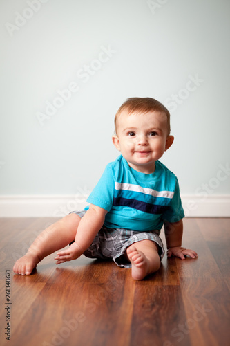 Happy Baby Boy Sitting on Wood Floor in Home
