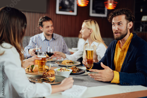 Young smiling Caucasian man dressed smart casual drinking beer and talking to his girlfriend. Restaurant intrerior.