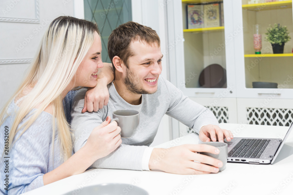 Young couple sitting at the morning in they kitchen and using laptop. Online shopping concept. Modern kitchen in background. Young couple sitting at the morning in they kitchen and using laptop. Online shopping concept. Modern kitchen in background.