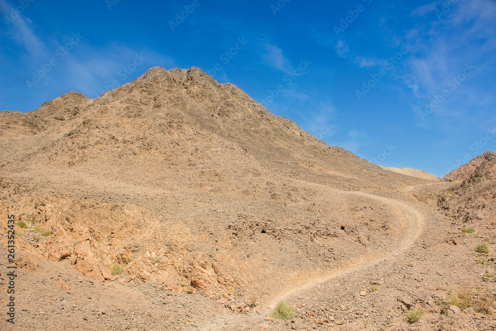 dry mountain in rocky desert outdoor wilderness natural environment scenic landscape with small trail for hiking and climbing, sand stones ground and vivid blue sky background