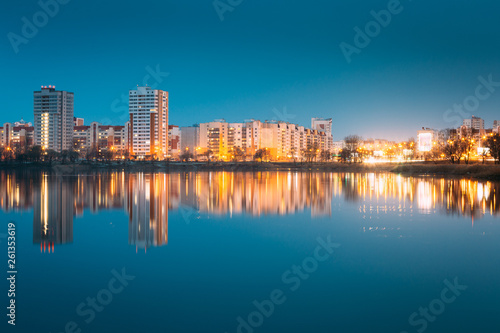 Night View Of Urban Residential Area Overlooks To City Lake Or River And Park In Evening Illumination, Reflecting In Water Surface.