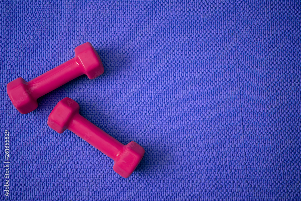 Top view of blue yoga mat with bright pink dumbbells with copy space Top view of blue yoga mat with bright pink dumbbells with copy space