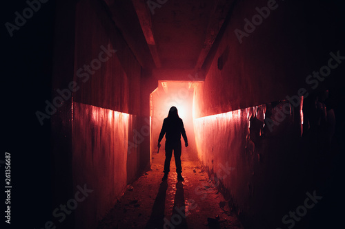 Creepy silhouette with knife in the dark red illuminated abandoned building. Horror about maniac concept photo