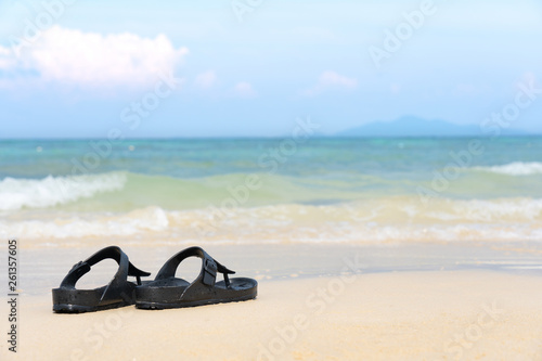 Sandal flip flop on the sand beach with blue ocean sea and sky background in summer vacation.Relaxing time on paradise.Travel,Holliday,Day off Concept. Copy space empty blank for text.