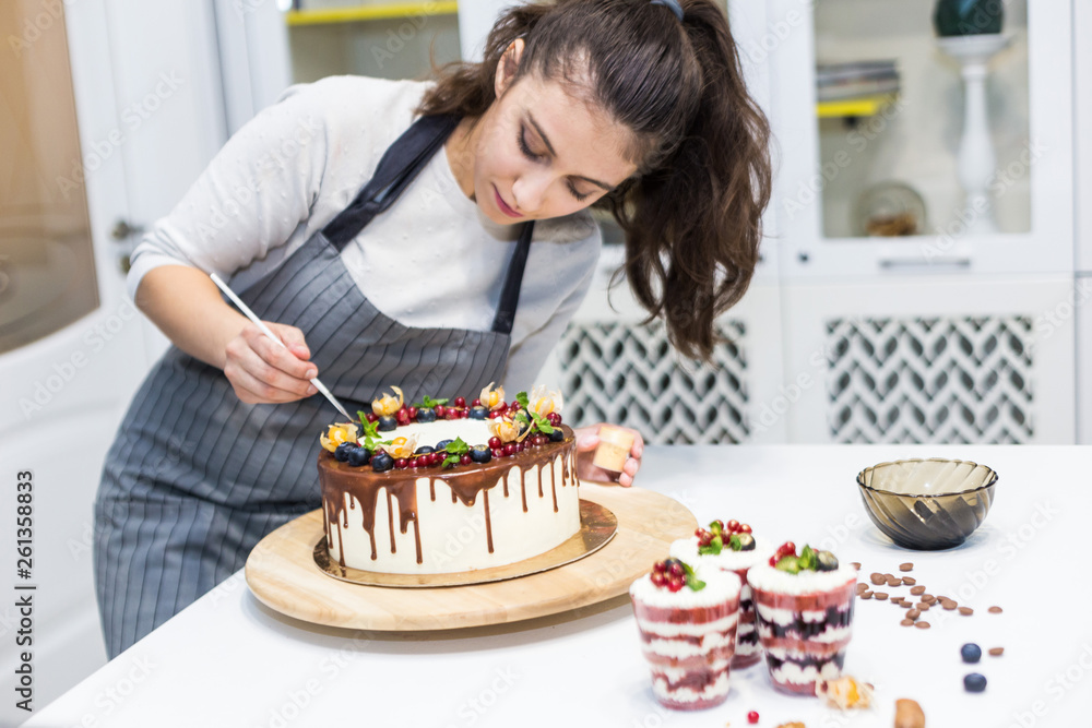 Fototapeta premium Decoration of the finished dessert. Pastry chef sprinkles confectionery with yellow powder. The concept of homemade pastry, cooking cakes.