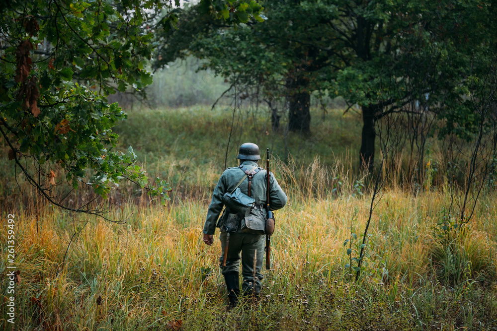 Single Re-enactor Dressed As German Wehrmacht Infantry Soldier In World War II Walking In Patrol Through Autumn Forest. WWII WW2 Times Single Re-enactor Dressed As German Wehrmacht Infantry Soldier In World War II Walking In Patrol Through Autumn Forest. WWII WW2 Times