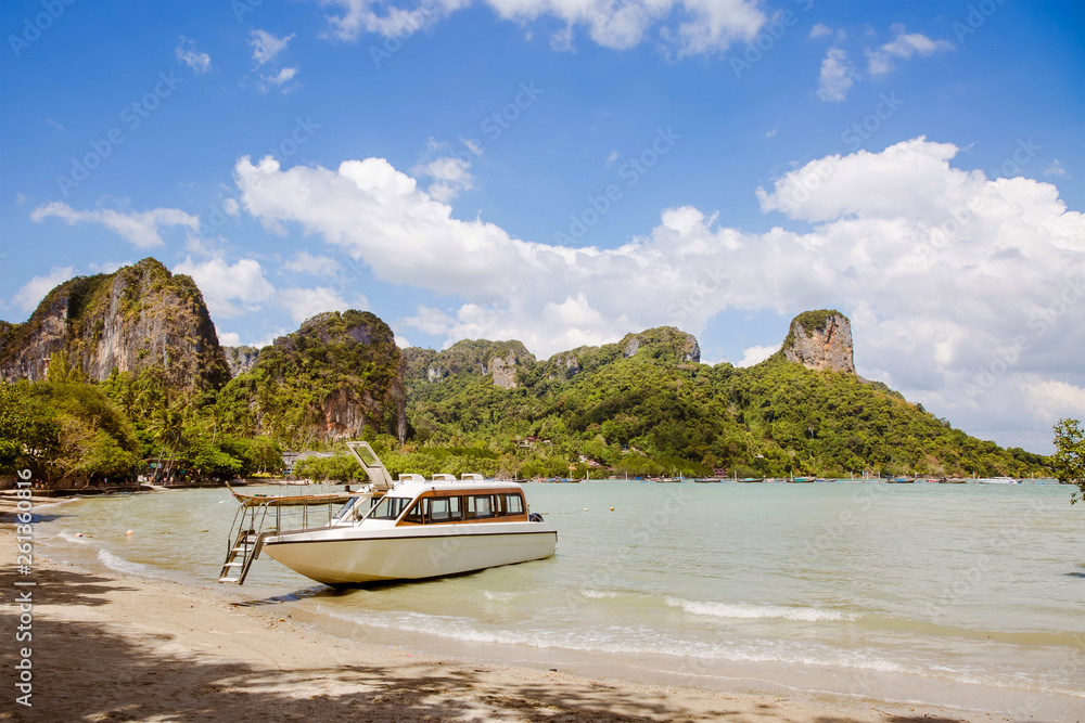 Snow white premium speedboat on the shore of a tropical island. Moored on a sandy beach, Tropics and rocks in the background. Krabi, railay