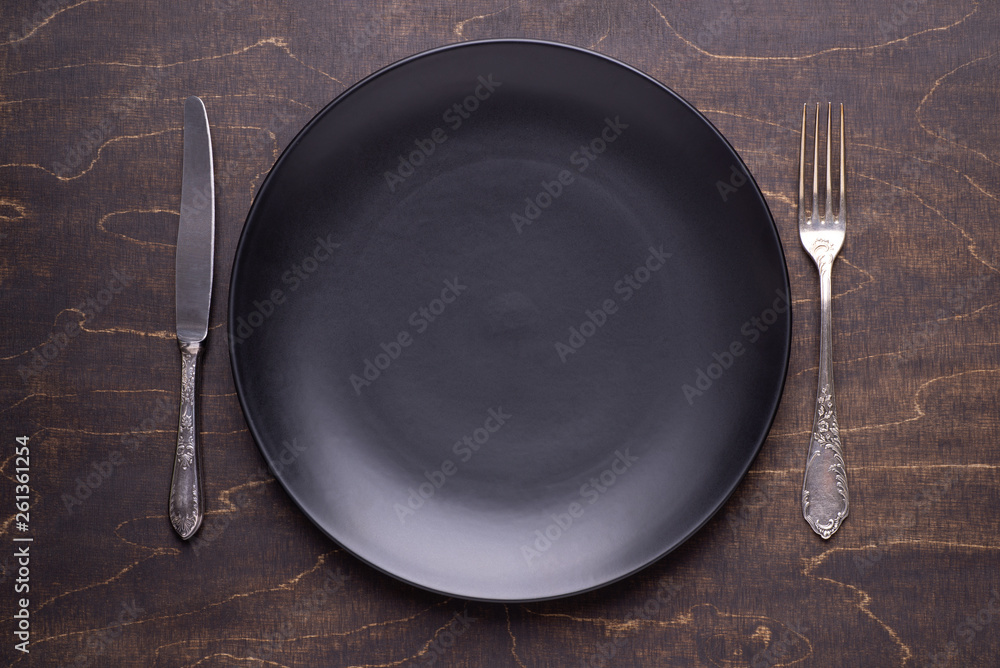Empty black plate and silver cutlery on dark wooden table, top view Empty black plate and silver cutlery on dark wooden table, top view
