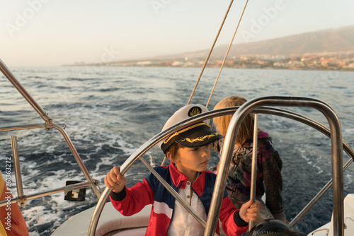 Positive kids in captain hat floating on expensive boat on sea in sunny day