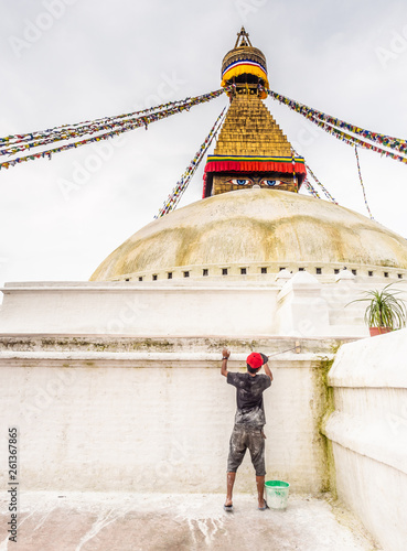 NEPAL, BOUDHANATH STUPA - AUGUST 19, 2014: Back view of young worker painting stone wall with lime wash photo