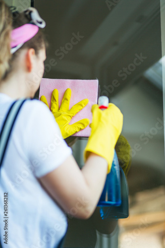 Young woman washing windows with yellow rubber gloves, cloth and cleaning product. 