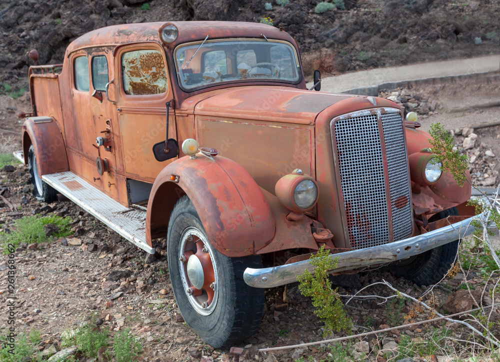 Front and side view of vintage rusting fire truck in desert.