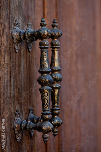 Ancient Italian metal door handles on brown wooden door.