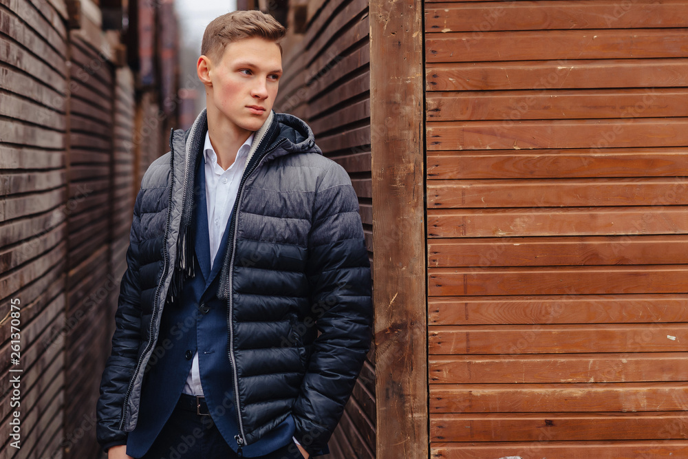 young stylish guy with a monumental face walks in a cool city near the wooden and stone walls young stylish guy with a monumental face walks in a cool city near the wooden and stone walls