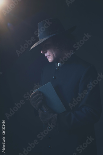 Mysterious victorian priest in hat holding book.