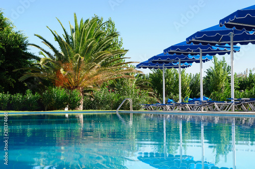 Palm and sun umbrellas by the pool, Greece. © delobol