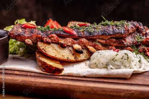 Delicious barbecued ribs seasoned with fresh herbs, cabbage salad, backed potato on an old rustic wooden chopping board