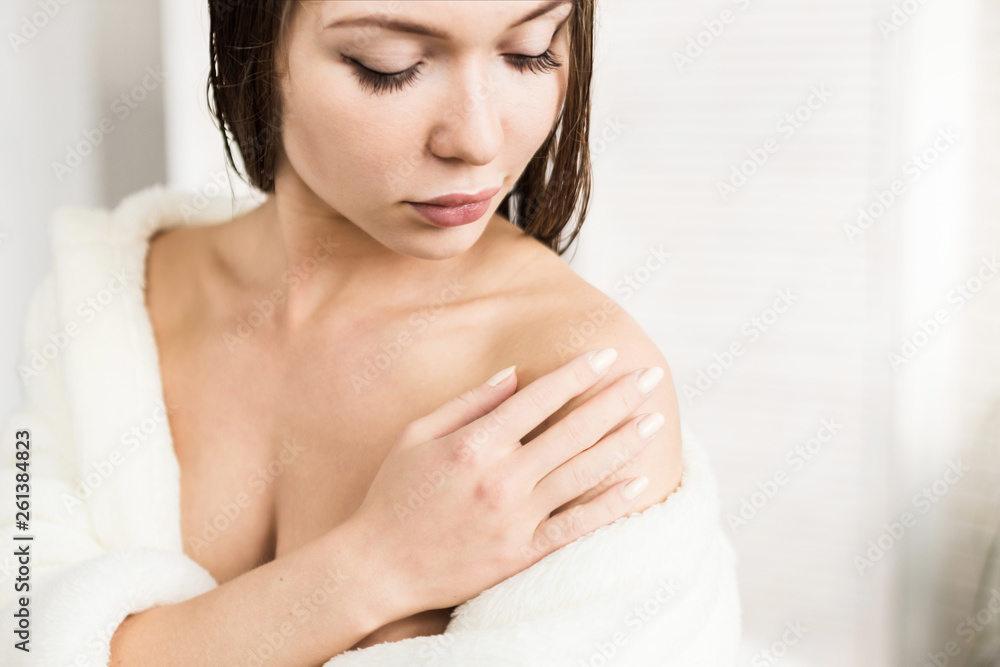 Attractive young girl in a white bathrobe applies cream to the skin while sitting in the interior of the bathroom and doing morning procedures. Skin and body care Attractive young girl in a white bathrobe applies cream to the skin while sitting in the interior of the bathroom and doing morning procedures. Skin and body care