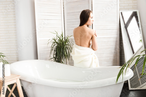 Attractive young girl in a white bathrobe applies cream to the skin while sitting in the interior of the bathroom and doing morning procedures. Skin and body care