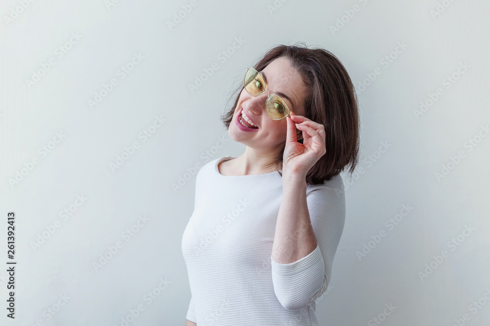 Simple studio portrait of hipster fashion smiling short-haired brunette girl in trendy yelow sunglasses isolated on white background. Fun positive young smart woman in glasses having fun smiling Simple studio portrait of hipster fashion smiling short-haired brunette girl in trendy yelow sunglasses isolated on white background. Fun positive young smart woman in glasses having fun smiling