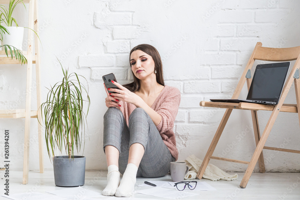 A happy woman in homemade casual clothes sits in a bright interior and uses a telephone, the girl is resting while working at a laptop and surfing the Internet. Cozy freelance work space, A happy woman in homemade casual clothes sits in a bright interior and uses a telephone, the girl is resting while working at a laptop and surfing the Internet. Cozy freelance work space,