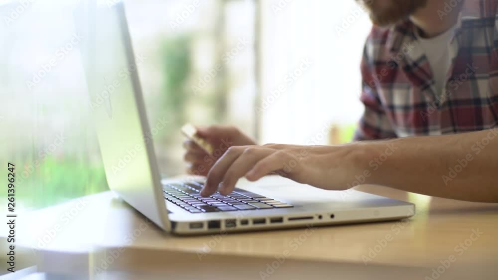 Mid section of excited young man using laptop while making online payment through credit card at home Mid section of excited young man using laptop while making online payment through credit card at home
