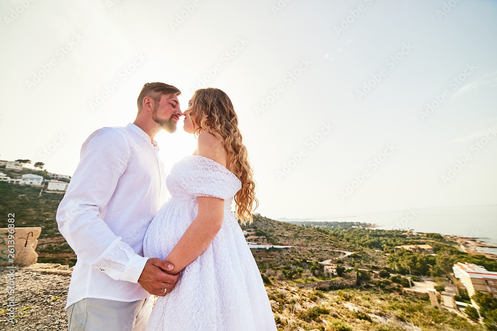 Young pregnant woman posing with her husband on a sunny summer day