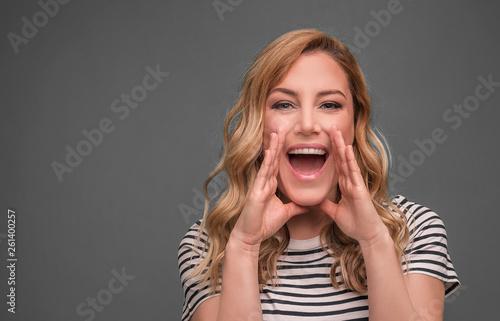 A woman screams with her arms folded. Beautiful young blonde on grey background.