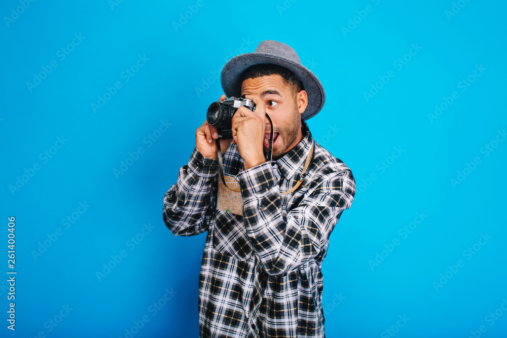 Portrait funny excited tourist guy in hat making photo on camera on blue background. Having fun, enjoying holidays, weekends, travelling around the world, expressing positivity Portrait funny excited tourist guy in hat making photo on camera on blue background. Having fun, enjoying holidays, weekends, travelling around the world, expressing positivity