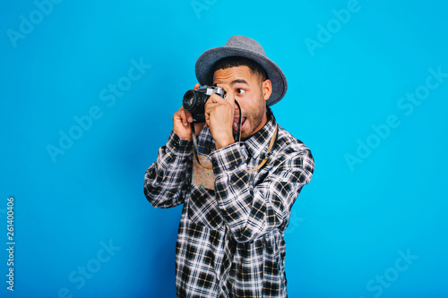 Portrait funny excited tourist guy in hat making photo on camera on blue background. Having fun, enjoying holidays, weekends, travelling around the world, expressing positivity