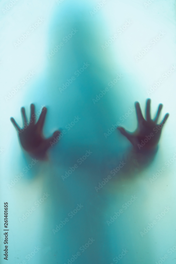 Blurred shadow of a horror woman. The hands on the glass. Dangerous person behind frosted glass. Person of mystery Halloween background. Fear, terror, mystery