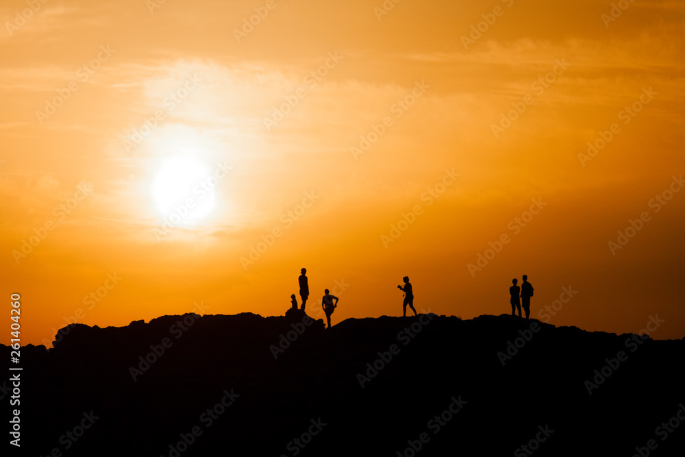 Black silhouettes of people standing on the top of a peak and watching sunset, sunrise. Mountain sunset, sunrise.