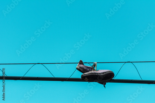 Sport tennis shoes tied on the electric wire against a clear blue sky.