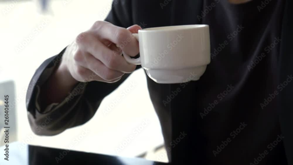 close-up view of coffee cup in hand of young man, he is sipping cappuccino and looking at camera close-up view of coffee cup in hand of young man, he is sipping cappuccino and looking at camera