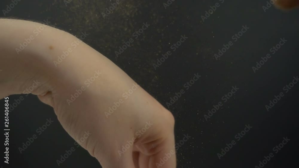 Makeup brush touching woman hand in slow motion. Golden color powder splashing by hitting wide brush for make-up to the wrist on a black background. Makeup brush touching woman hand in slow motion. Golden color powder splashing by hitting wide brush for make-up to the wrist on a black background.