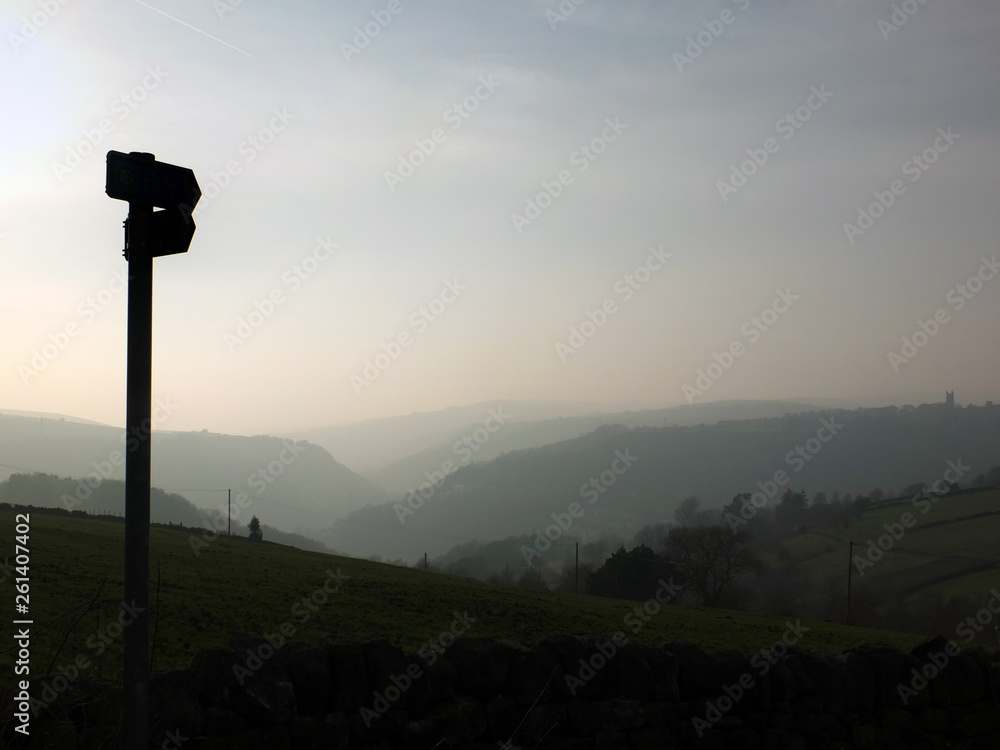 a direction sign in silhouette over misty landscape at daybreak with mist covered hills and valley just before sunrise