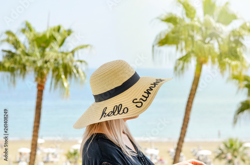 Young caucasian women  having a straw hat on his  head  relaxing     in a hotel balcony on the seashore. looking at   the blue sky horizon and palm tree.Summer holidays . Bright warm filter . © SnowMan