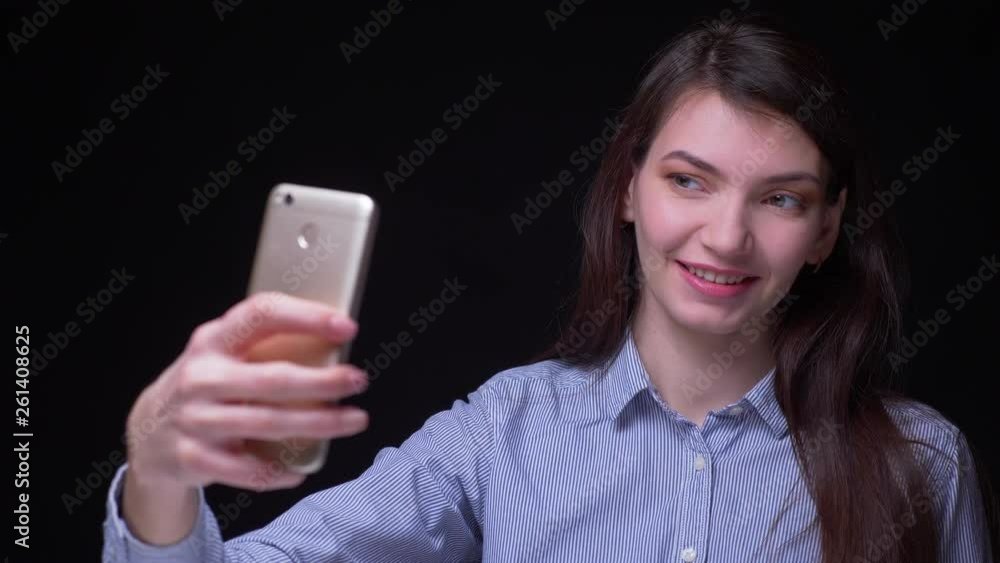 Pretty brunette businesswoman in blue blouse making selfie-photos using smartphone being happy at black background. Pretty brunette businesswoman in blue blouse making selfie-photos using smartphone being happy at black background.